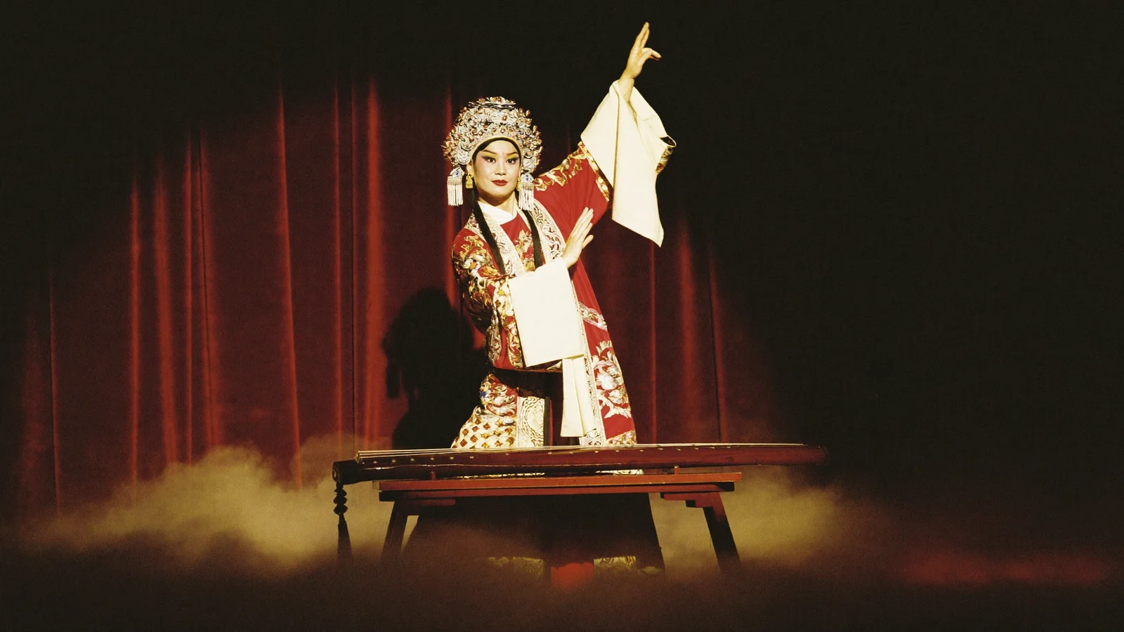An elaborately costumed Cantonese opera performer on a traditional stage with an ornate backdrop and warm spotlight, evoking the qin and the Wei-Jin era aesthetic, illustrative image for this Ancient Tune of Guangling opera guide at Sha Tin Town Hall, not a photo of the actual cast or production