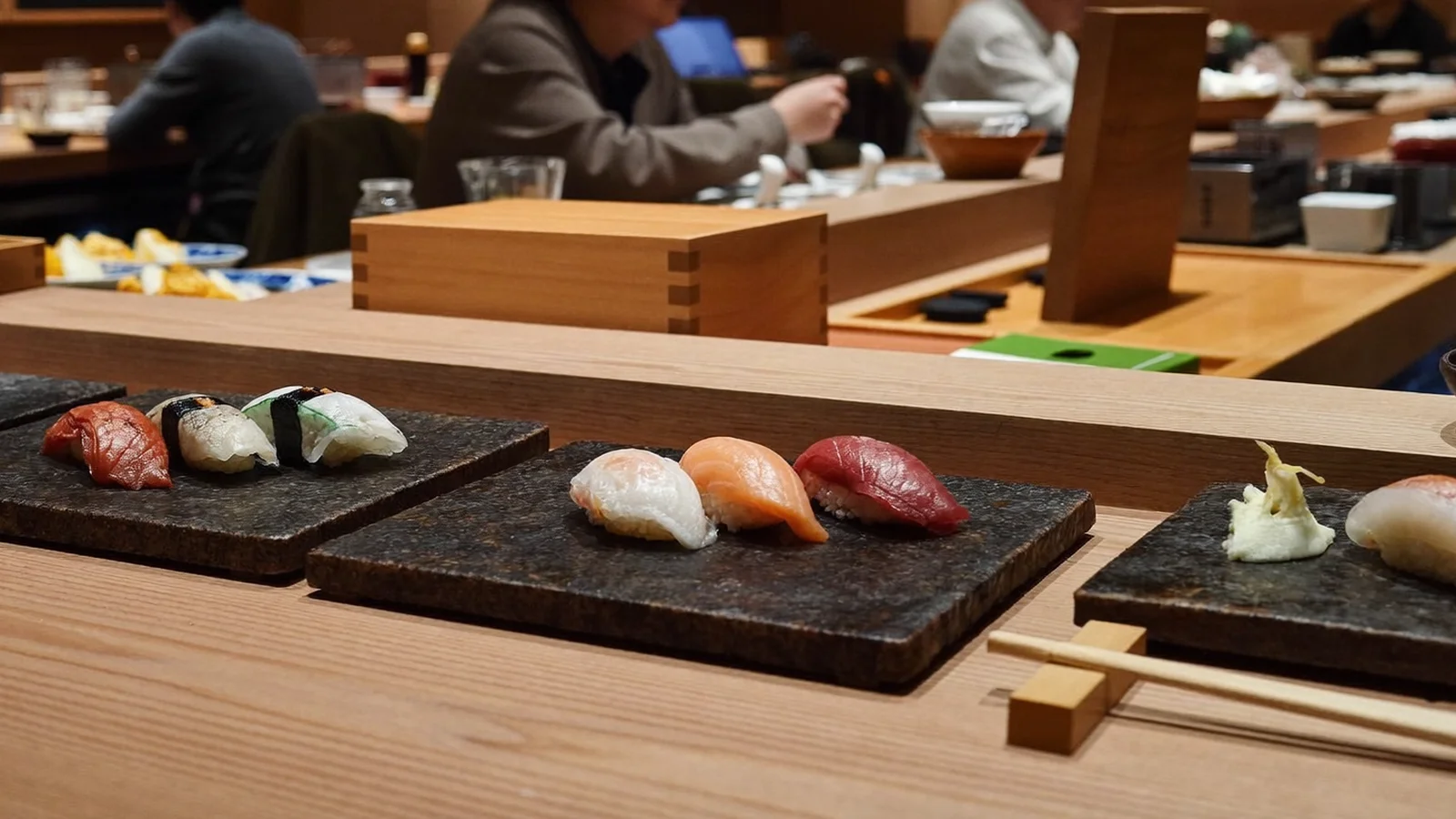 An elegant modern Japanese restaurant counter with fresh sashimi, sushi and seafood artfully plated, local Hong Kong Chinese diners softly blurred in the background, illustrative image for this K11 MUSEA restaurant guide, not a photo of the actual venue