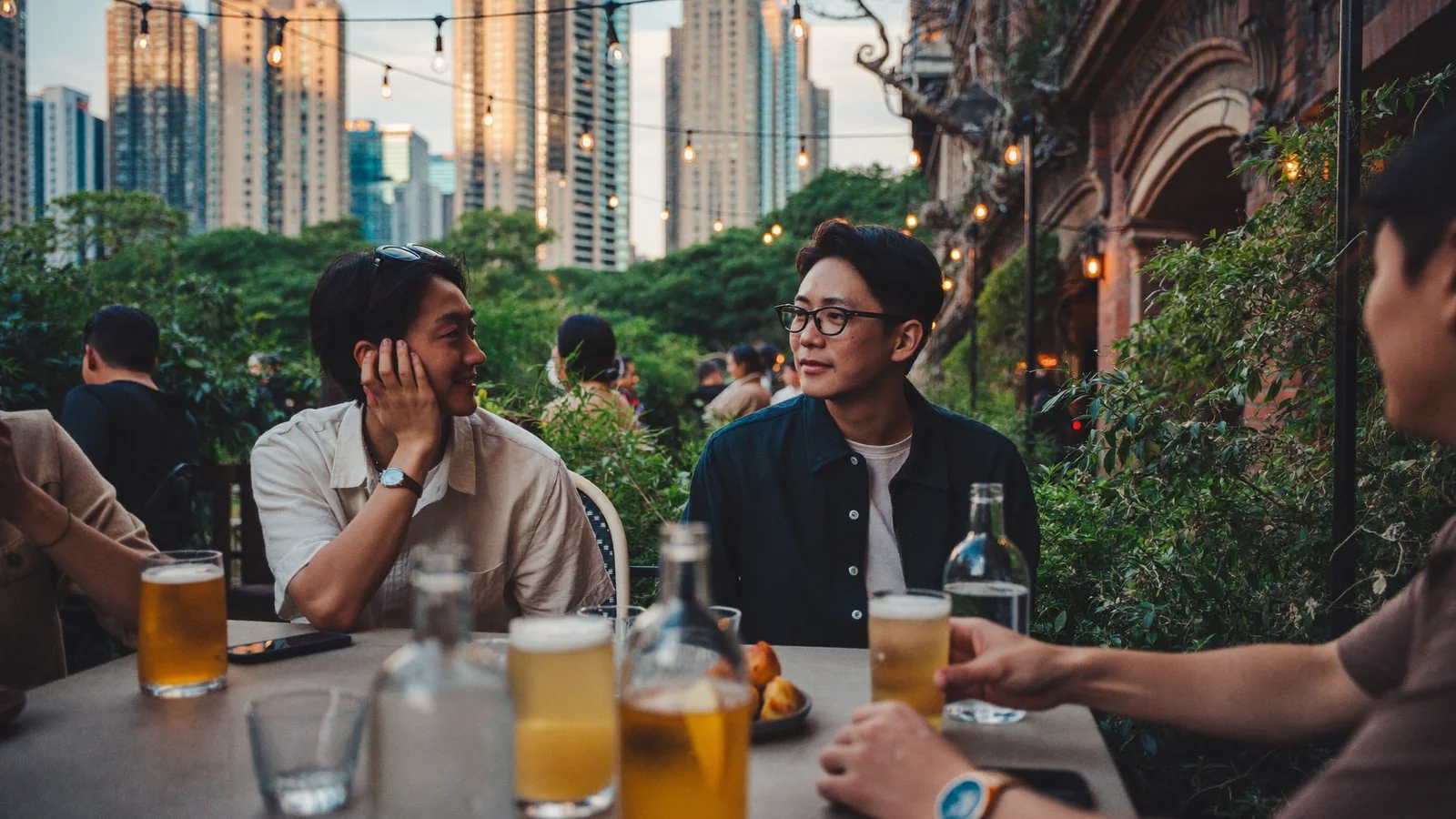 本地香港朋友喺黃昏時分喺戶外露台酒吧嘆啤酒，背後係城市天際線 —— 此為香港露天酒吧指南嘅示意圖片，並非任何特定場地嘅實照