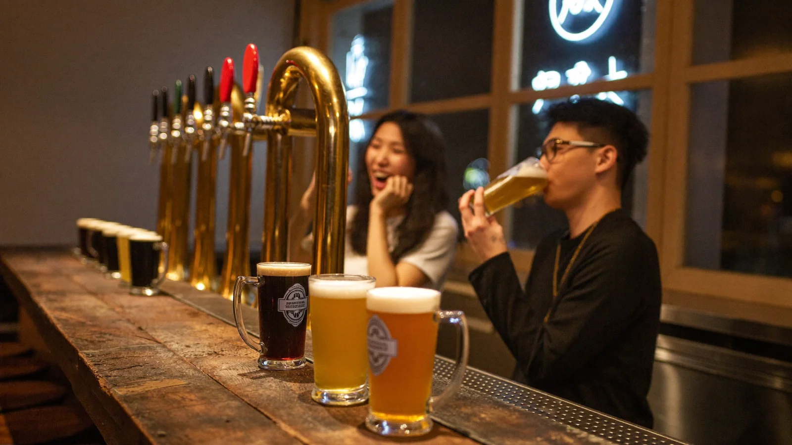 Friends sharing craft beer at a Hong Kong taproom bar lined with brass taps and a tasting flight - illustrative hero for this craft beer guide, not a photo of a specific bar