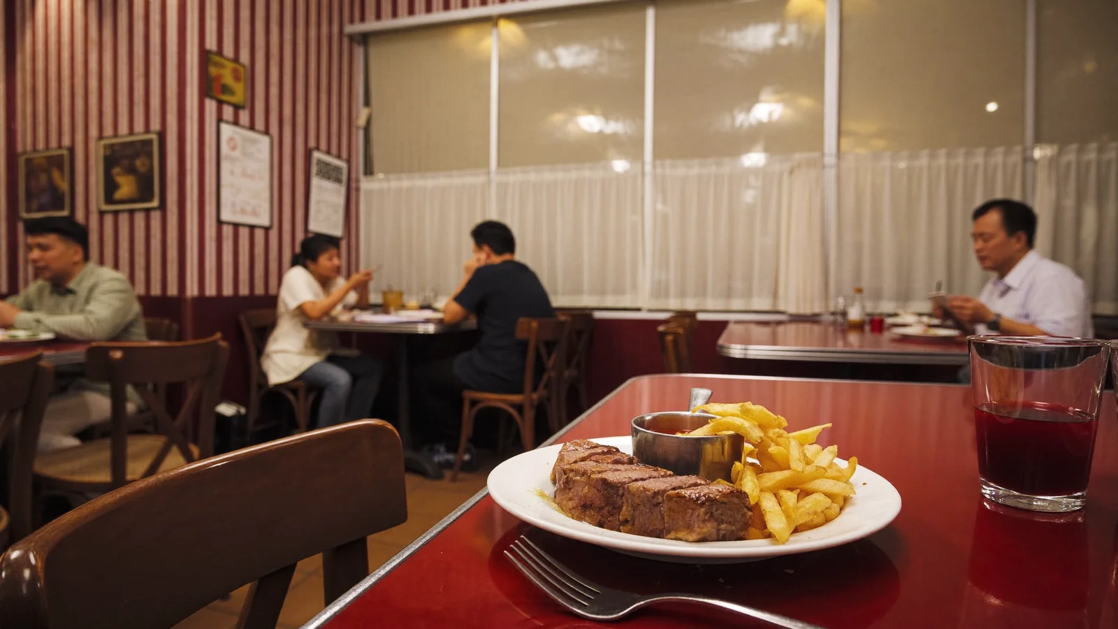 A French bistro dining room with burgundy-striped walls, red tables and a plate of steak frites, illustrative image for this Bistrot's Suzette Kai Tak restaurant guide, not a photo of the actual restaurant interior