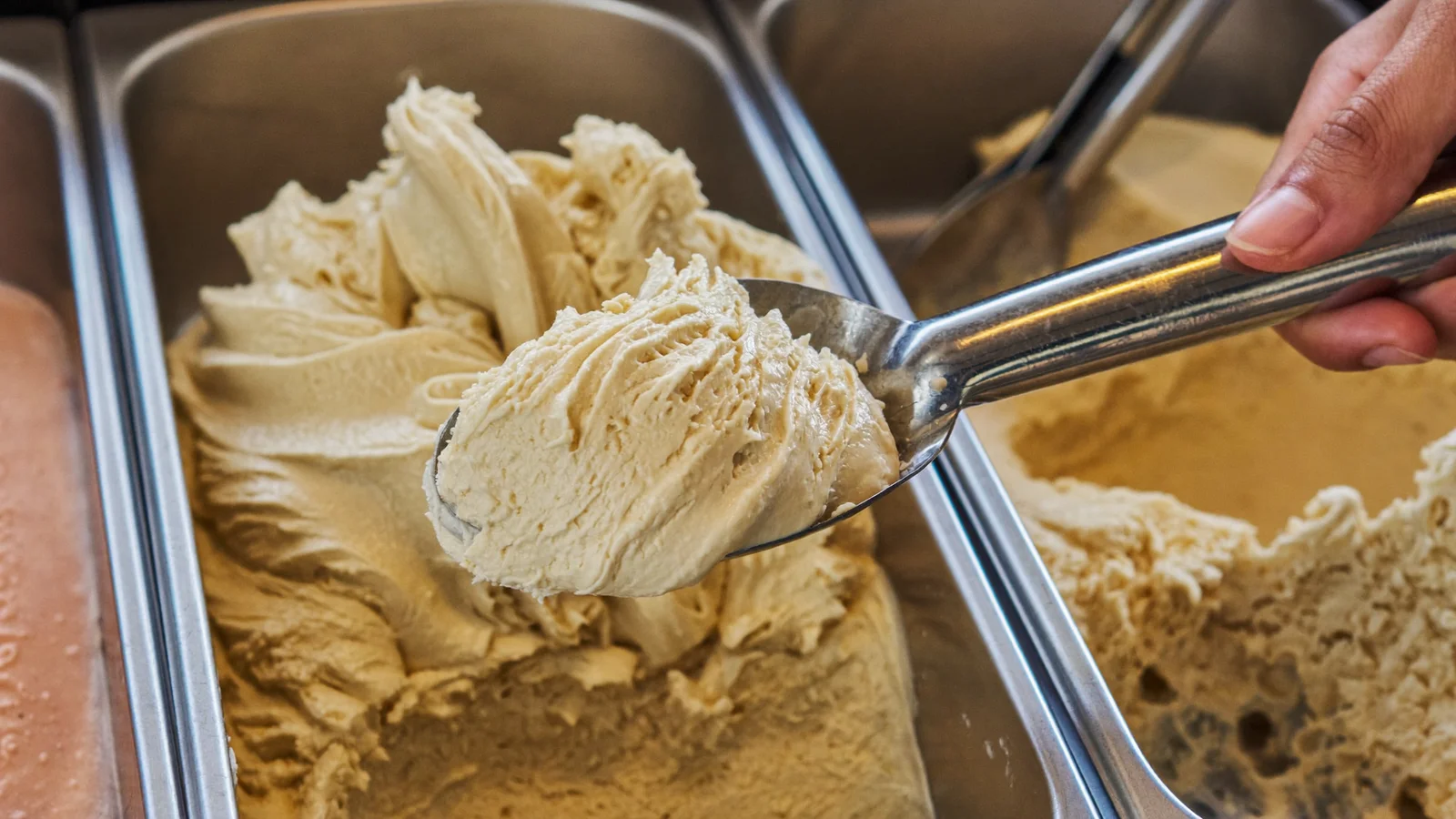 Illustrative image of a gelato spade scooping dense, creamy gelato from a stainless steel pan, not a photo of the actual venue