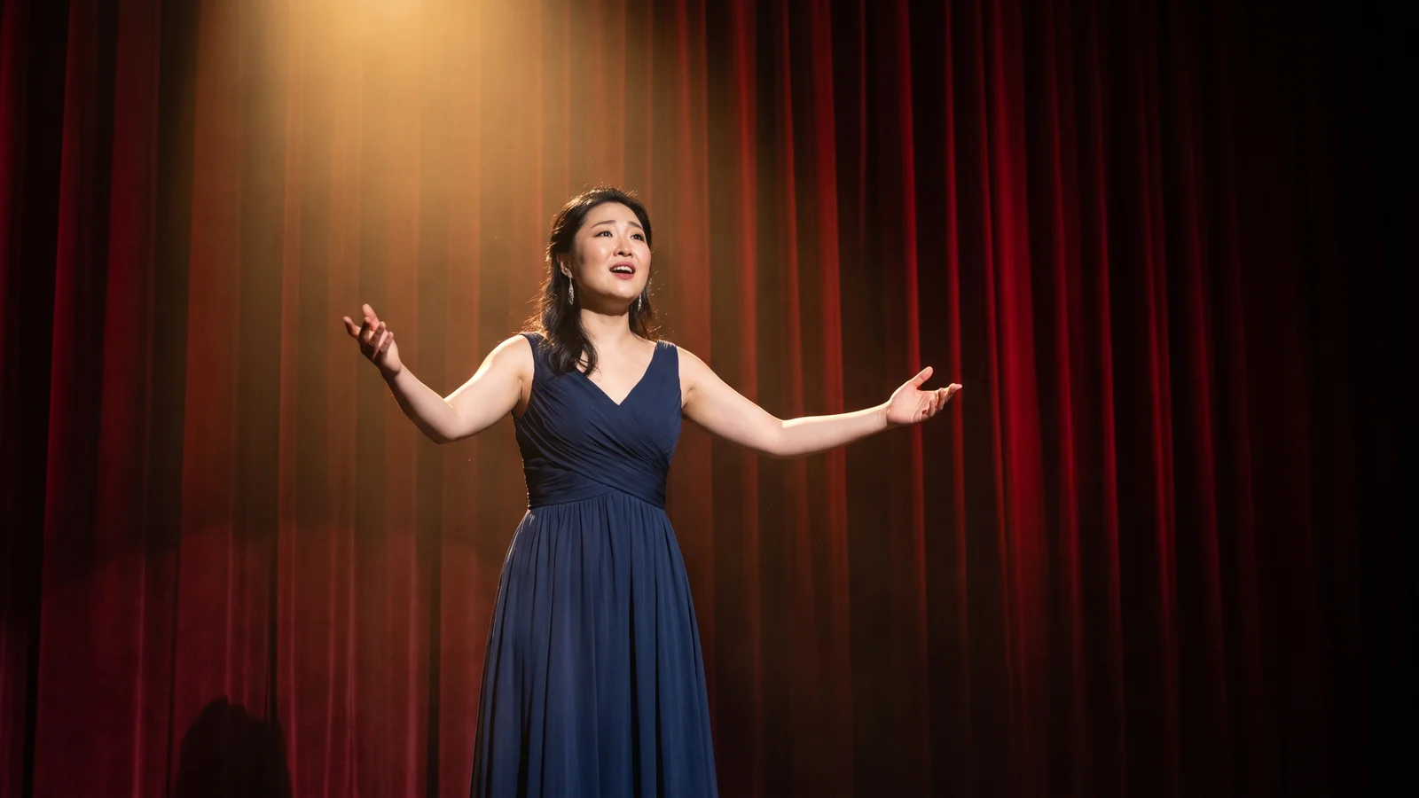 A dramatically lit opera stage with a lone performer in a flowing costume against a deep red curtain backdrop, illustrative image for this Cavalleria Rusticana and Pagliacci opera guide, not a photo of the actual Opera Hong Kong production or singers