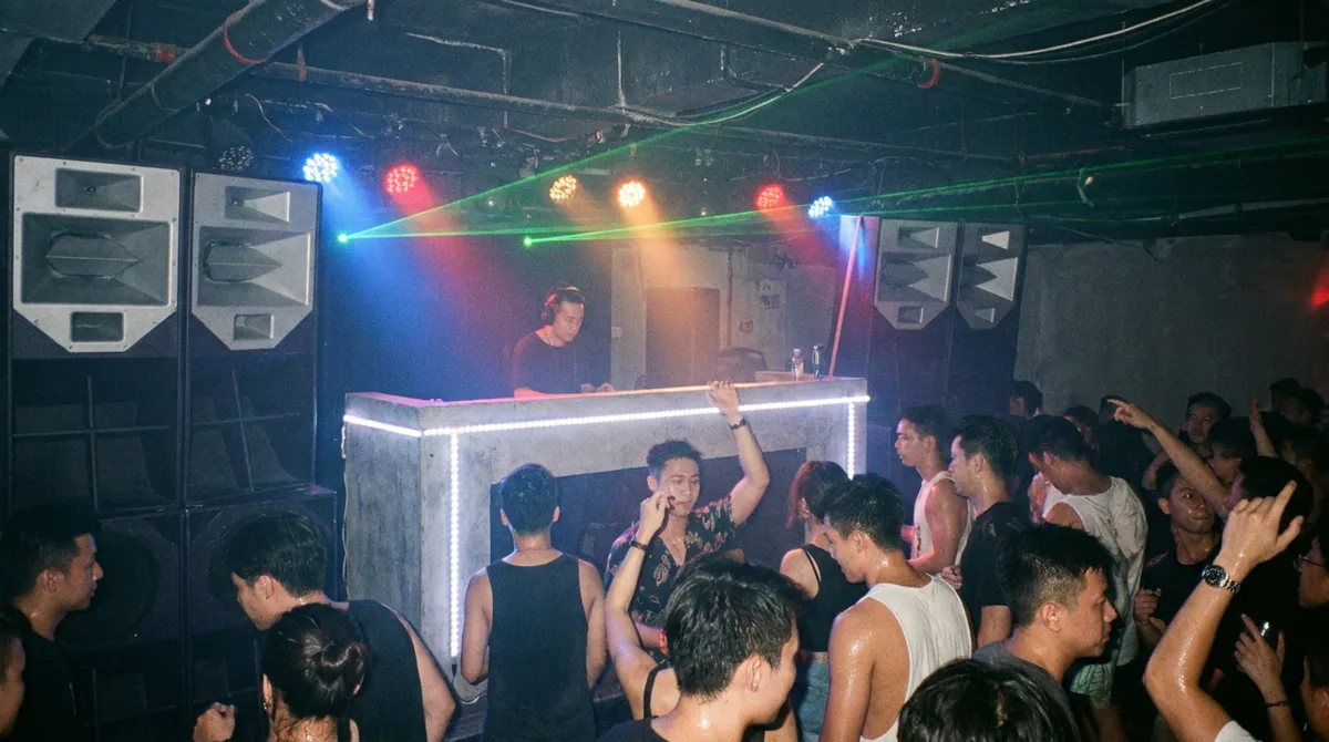 Packed Hong Kong underground nightclub dance floor with a DJ behind a glowing booth and dramatic strobe and laser lighting