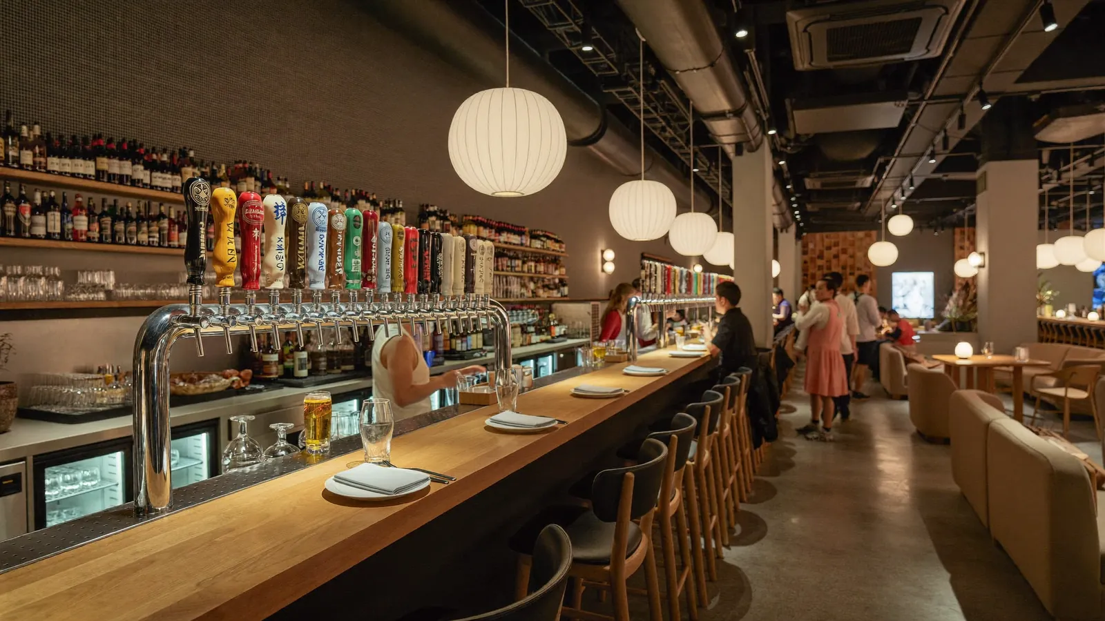 A warm, spacious bar-restaurant interior with craft beer taps and relaxed social seating, illustrative image for this Commune Causeway Bay guide, not a photo of the actual venue