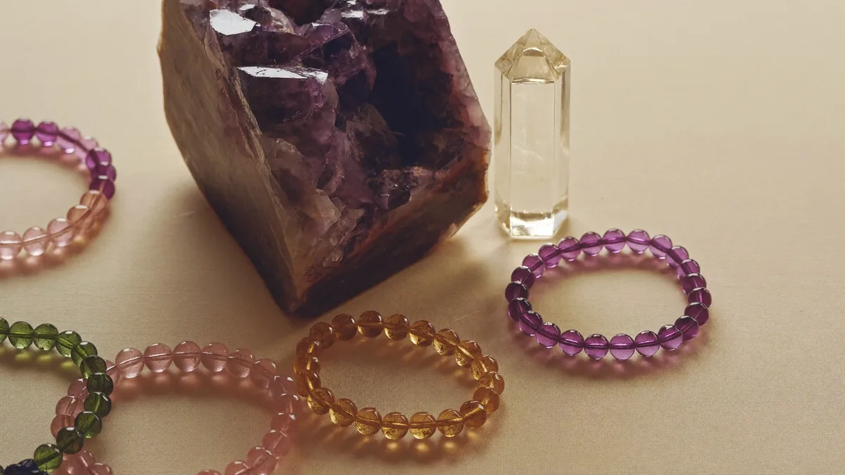 Natural crystal bracelets, a raw amethyst cluster and a clear quartz point arranged in warm light, evoking Crystale's natural-crystal jewellery in Hong Kong