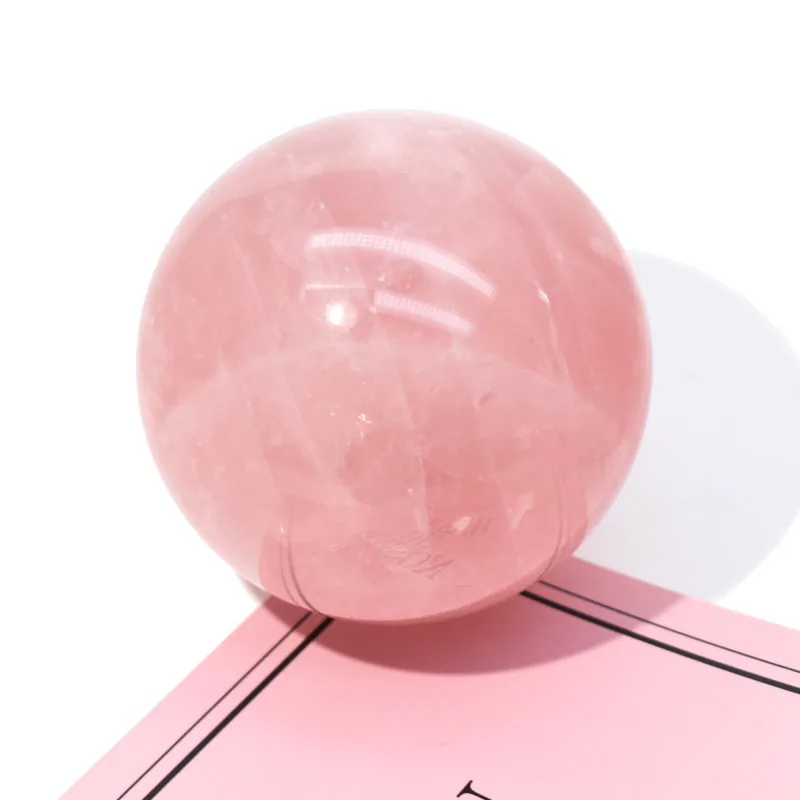 A polished rose quartz crystal sphere photographed on a soft pink surface, sold by Crystale in Hong Kong