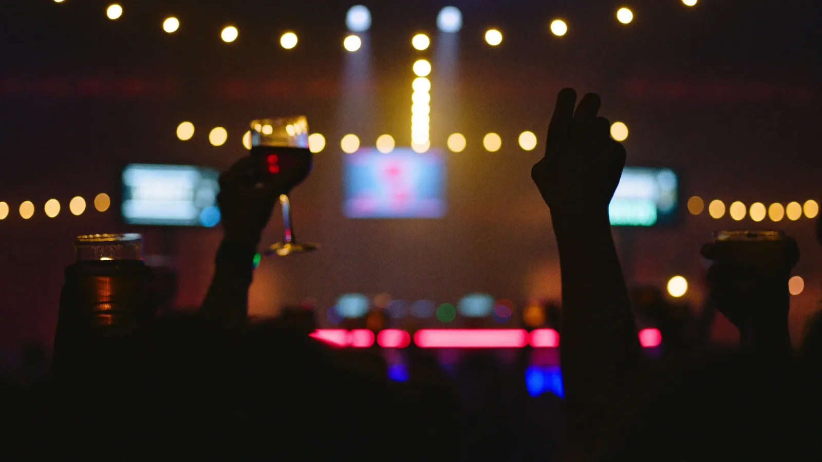 A moody, warmly lit late-night hotel bar with a DJ booth glowing under coloured stage lights and a crowd dancing with drinks in hand, illustrative image for this Eaton HK Cantopop party guide, not a photo of the actual venue, DJs or event