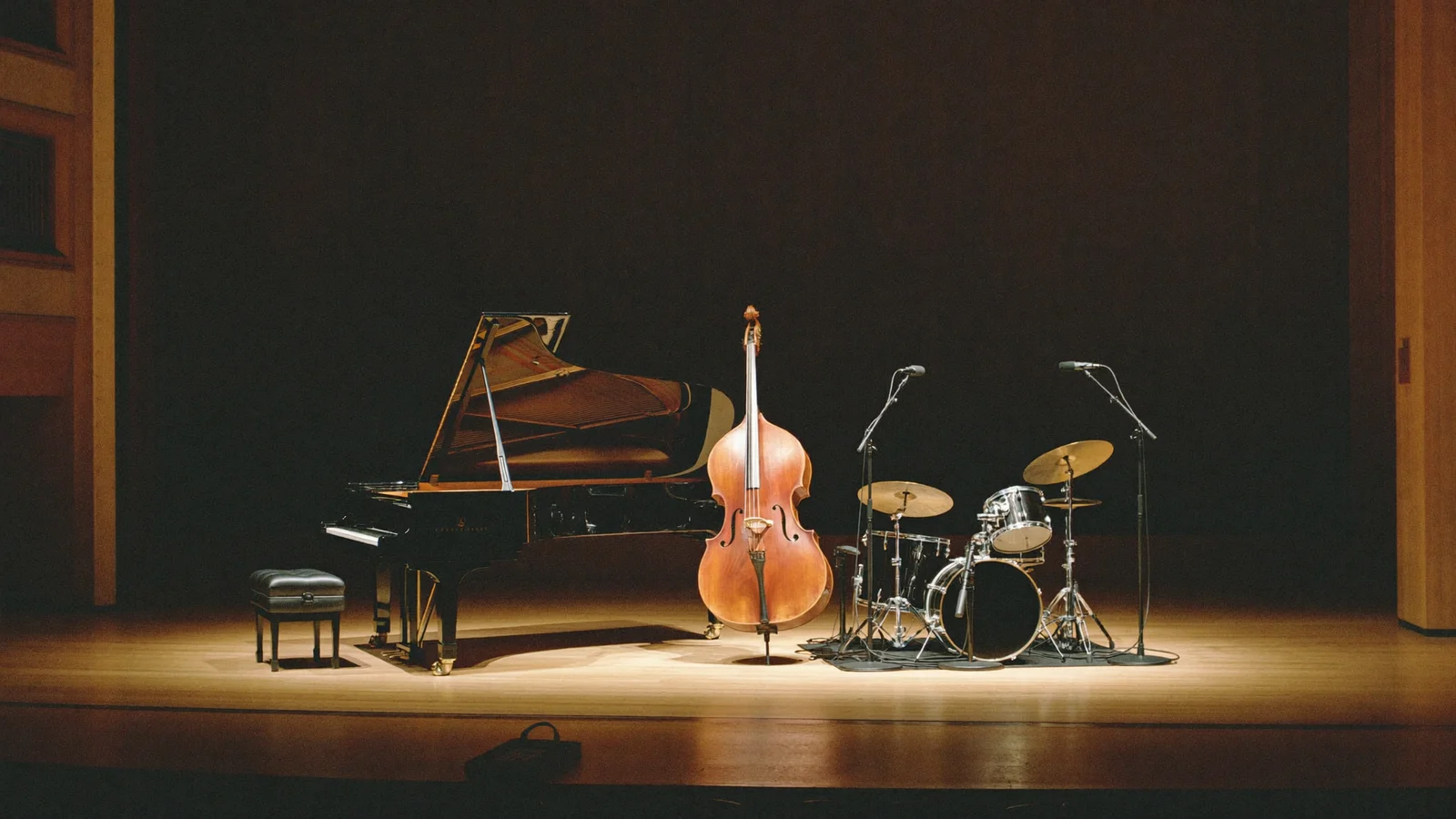 A grand piano, double bass and drum kit lit softly on a bare theatre stage, illustrating a guide to the Espen Eriksen Trio Nordic jazz concert in Hong Kong - an illustrative image, not a photo of the actual performance