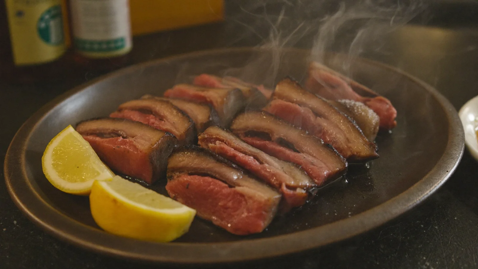 Thick-cut charcoal-grilled beef tongue slices with lemon wedges on a dark plate at a Japanese grill counter, illustrative image for this Gyutan Valley guide, not a photo of the actual venue