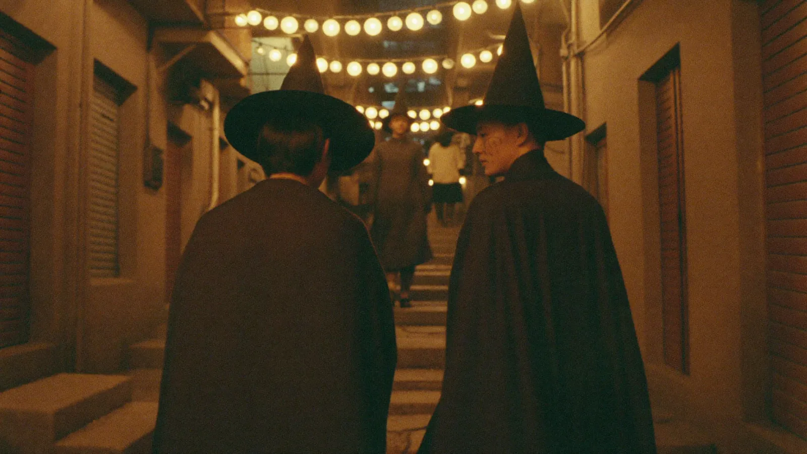 A narrow sloping lane at night lit by warm lanterns as a few people in dark Halloween costumes walk uphill, an illustrative image for this Halloween nightlife guide and not a photograph of a named venue