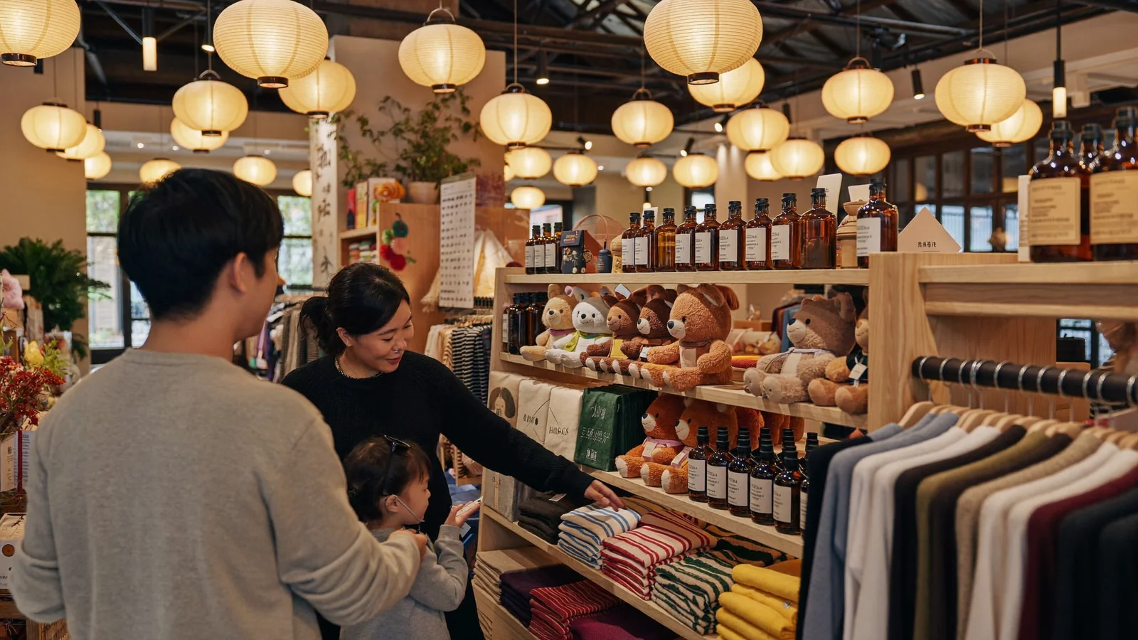 A warmly lit, lantern-strung themed pop-up shop with plush toys and striped scarves on wooden shelves, a family browsing - an illustrative hero image for this guide to the Harry Potter Mahou Dokoro pop-up, not a photo of the actual store