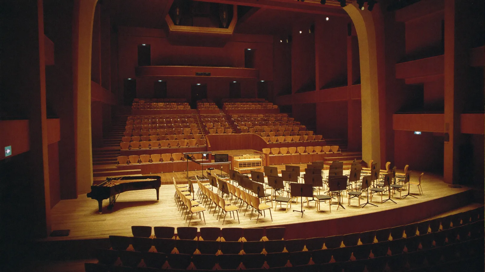 The empty, dramatically lit stage of a grand concert hall with orchestral chairs and music stands arranged under warm golden stage lighting, illustrating a guide to the HK Phil Season Opening concert - an illustrative image, not a photo of the actual performance