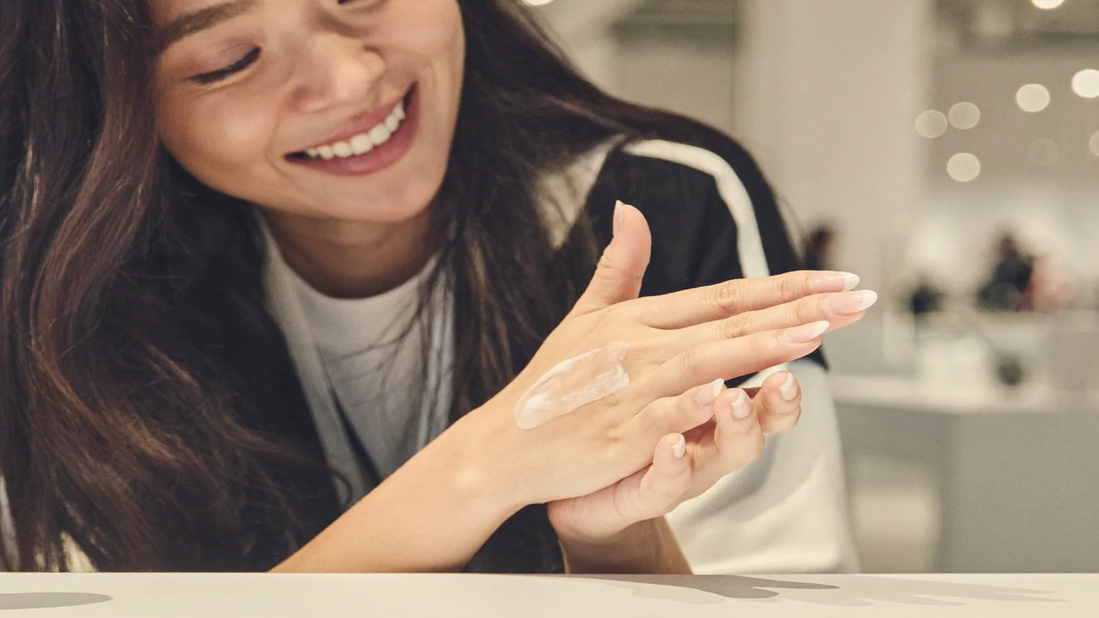 A smiling local Hong Kong woman testing skincare cream on her hand at a bright beauty fair counter - illustrative hero for this Hong Kong Beauty and Wellness Expo guide, not a photo of the actual event