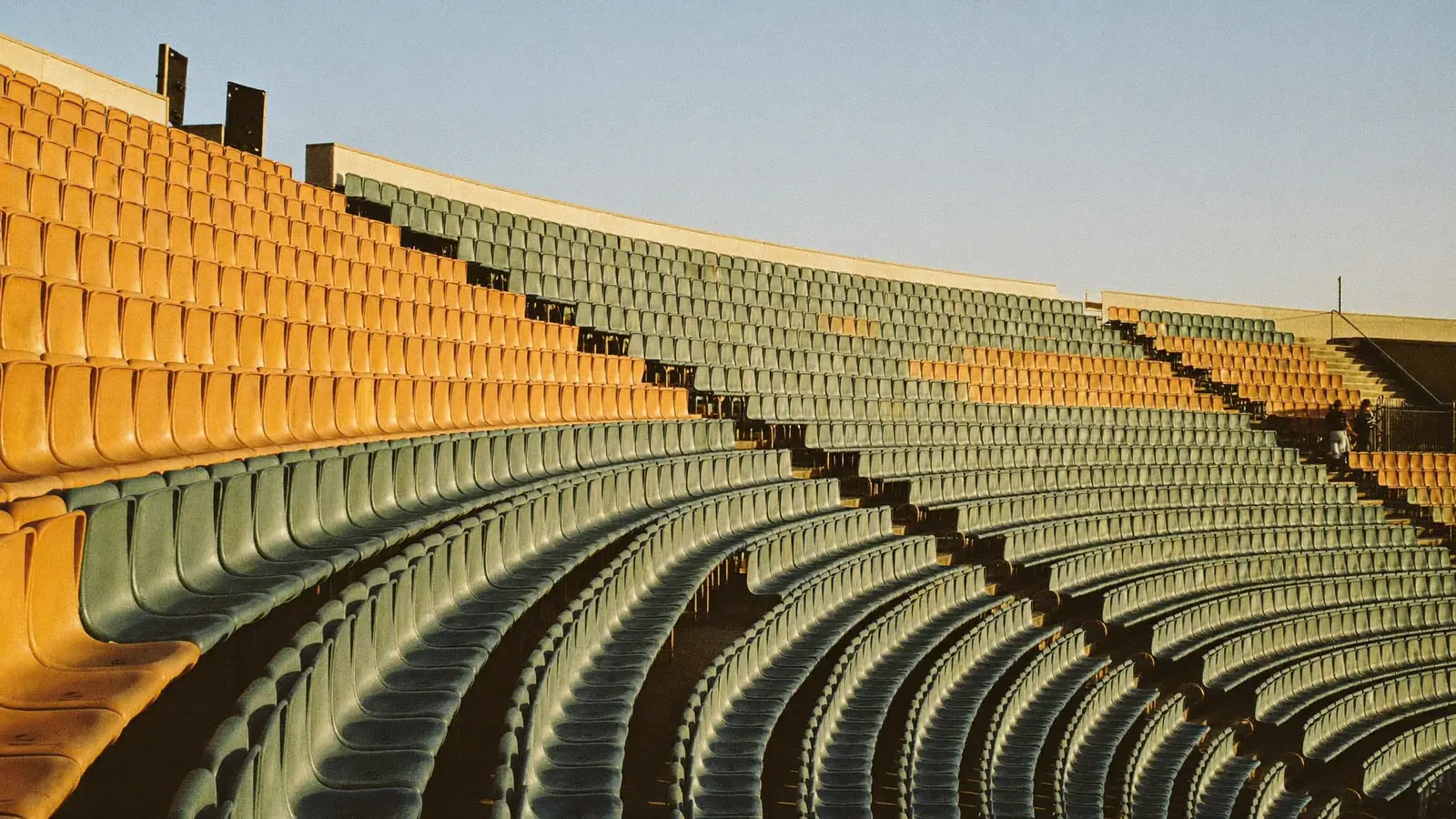 An illustration of long curved rows of empty stadium seats in low evening sunlight, introducing a guide to postponed Hong Kong concerts and how their refunds work. It is not a photograph of a named venue.