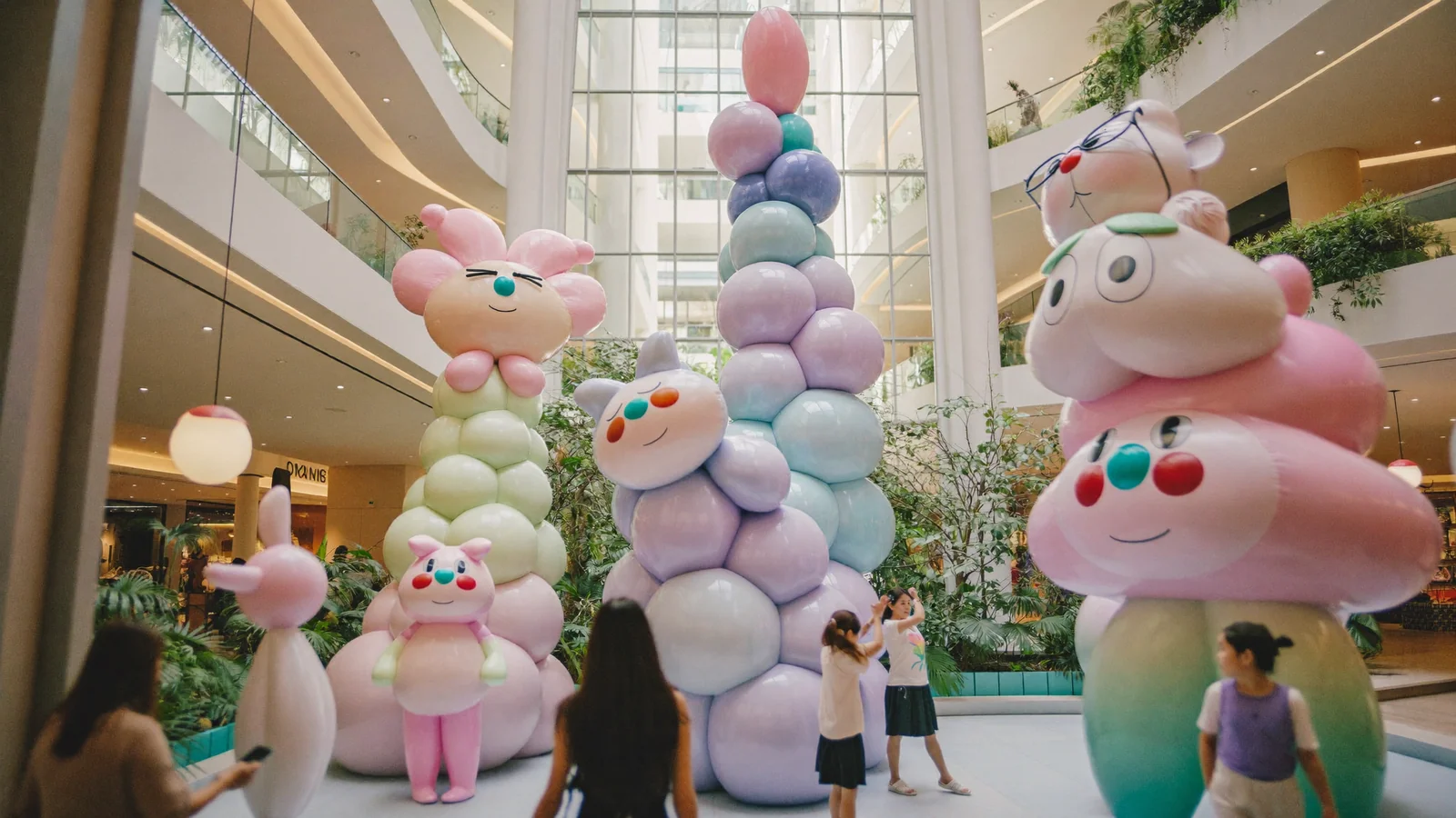 A whimsical shopping-mall atrium art installation of oversized pastel plush characters with visitors taking photos - an illustrative hero image for this guide to juju world at Pacific Place, not a photograph of the actual installation