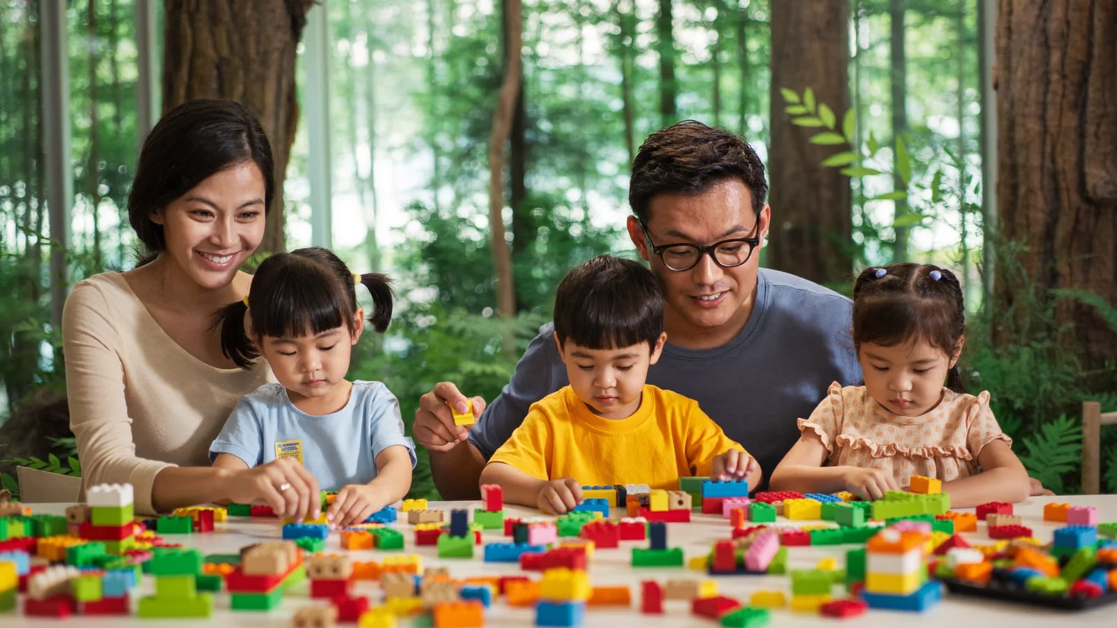 A family with young children building colourful LEGO bricks together at a play table inside an indoor family attraction - an illustrative hero image for this LEGOLAND NINJAGO Hong Kong guide, not a photo of the actual venue