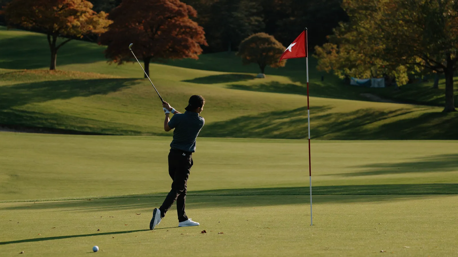 A local Hong Kong Chinese golfer mid-swing on an open fairway at a golf course in the New Territories, warm autumn afternoon light, green hills in the background, illustrative image for this Link Hong Kong Open 2026 guide, not a photo of any specific player or tournament round