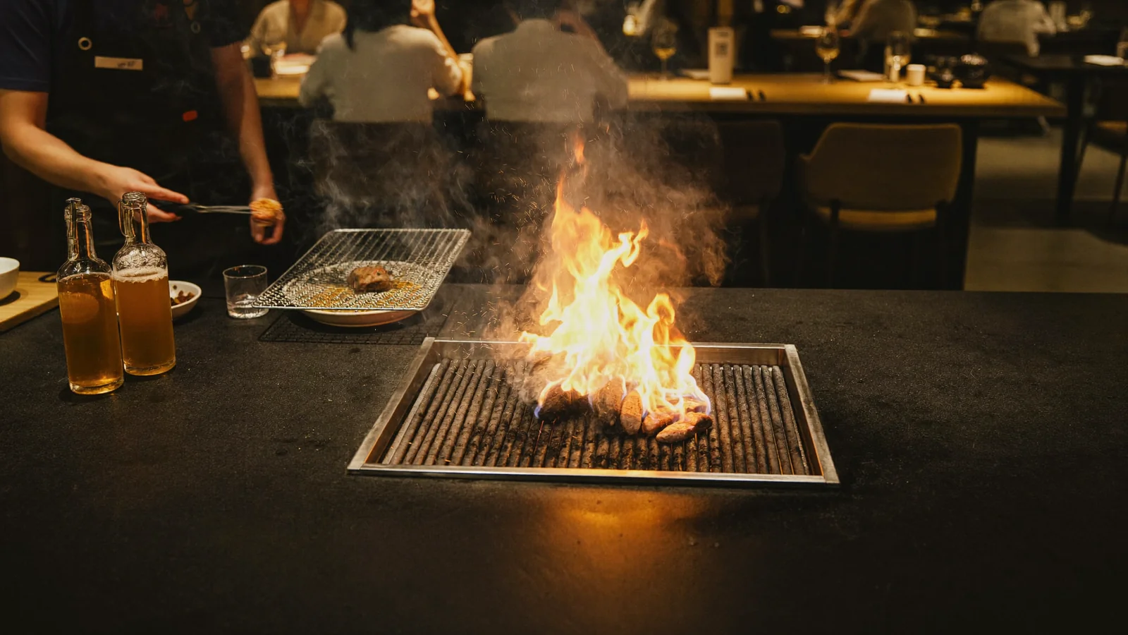 An open-fire grill with live flames and a chef cooking over the hearth in a moody dining room - an illustrative hero image for this guide to the Marrow pop-up in Wan Chai, not a photo of the actual restaurant