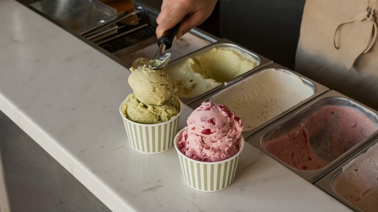 大理石吧枱上一杯色彩繽紛嘅雙球雪糕，於時尚香港gelato店內特寫拍攝，此為Messina x Mius聯乘指南嘅示意圖片，並非實際產品相片