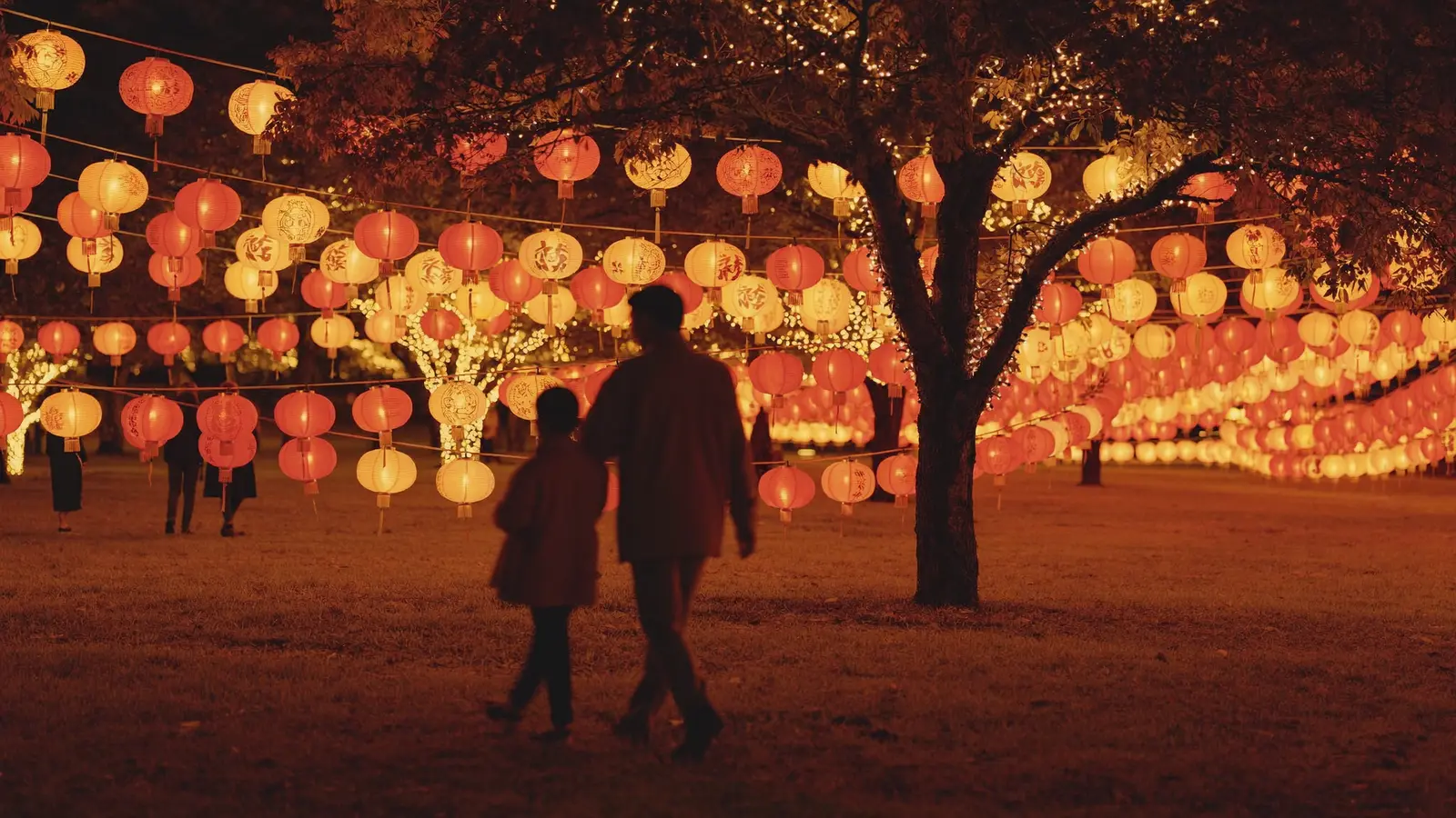 Glowing, oversized paper lanterns illuminated at night in a Hong Kong park with silhouettes of families walking past, illustrating a guide to the Victoria Park Mid-Autumn Lantern Carnival - an illustrative image, not a photo of the actual event