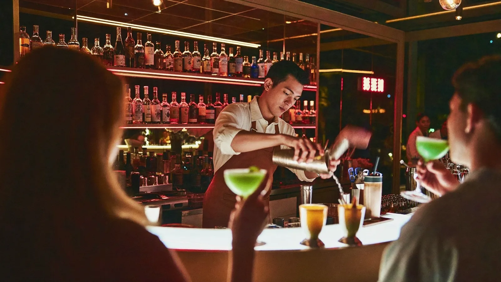 A moody, neon-lit cocktail bar with a bartender mixing a drink behind the counter - illustrative hero for this Hong Kong cocktail menu guide, not a photo of either bar itself