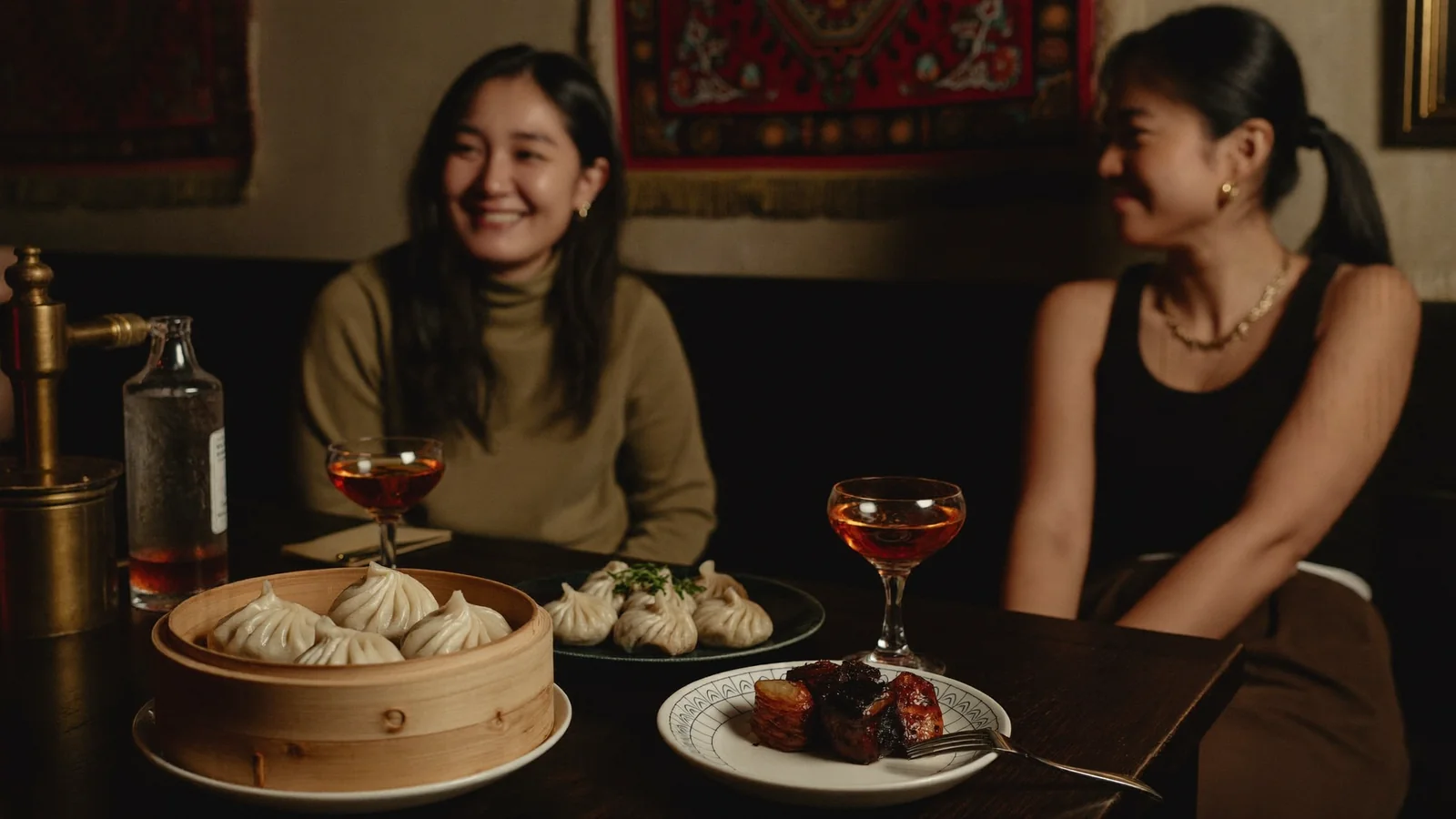 An intimate, dimly lit Nepalese speakeasy table with a steamer of momos, grilled meat and cocktails - illustrative hero for this Hong Kong Niwas guide, not a photo of the venue itself