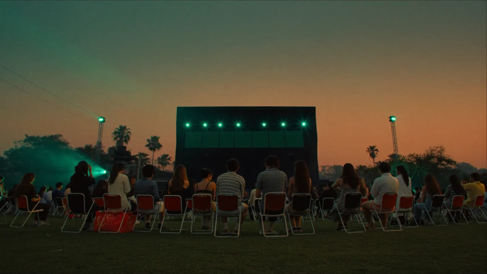 Silhouetted outdoor concert crowd on a grassy lawn facing a distant lit stage at dusk - an illustrative image for this Simple Plan West Kowloon ticket guide, not a photograph of the show