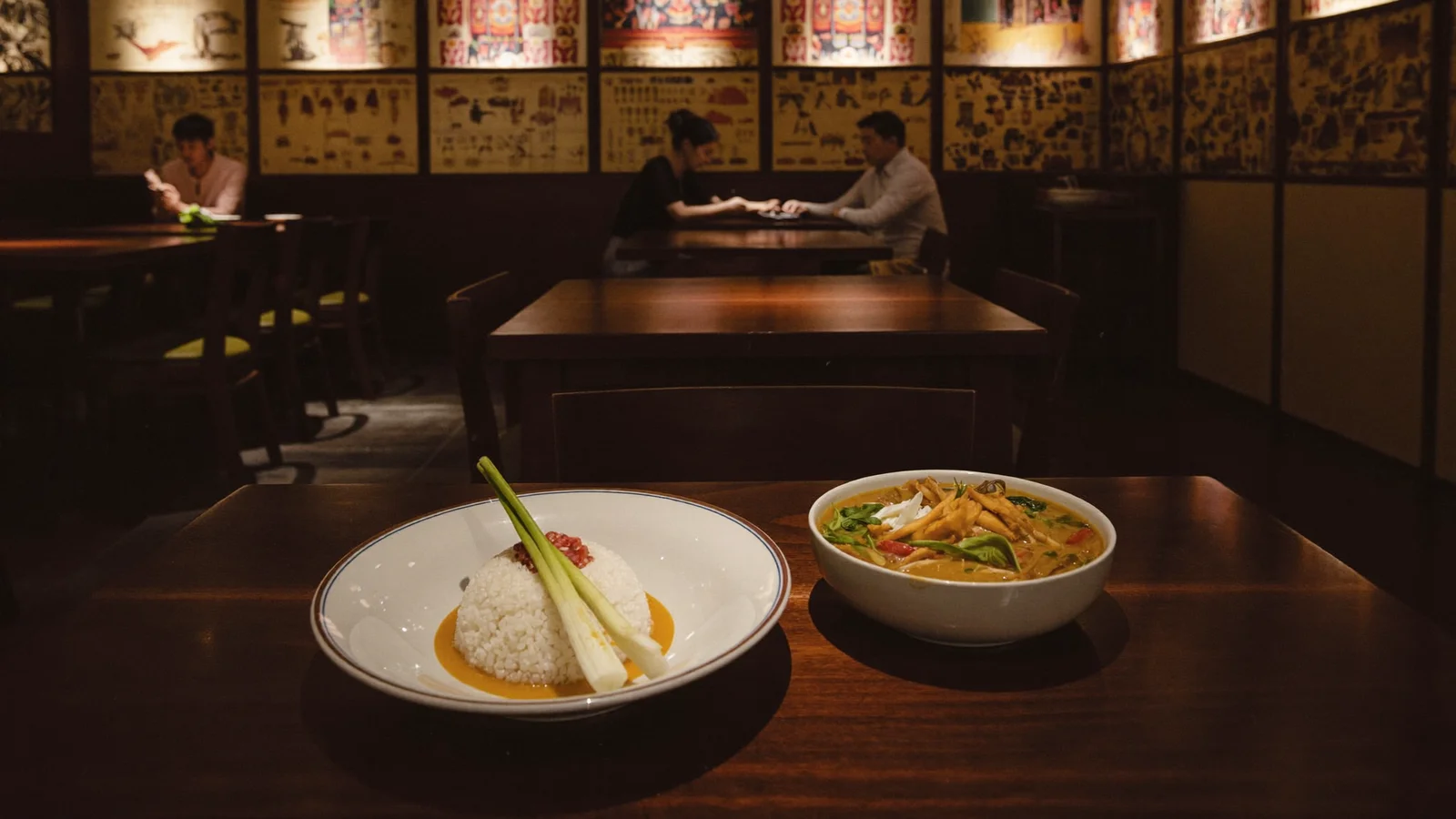 Illustrative image of a moody, warmly lit Thai restaurant interior with wooden accents and vintage motifs, not a photo of the actual venue