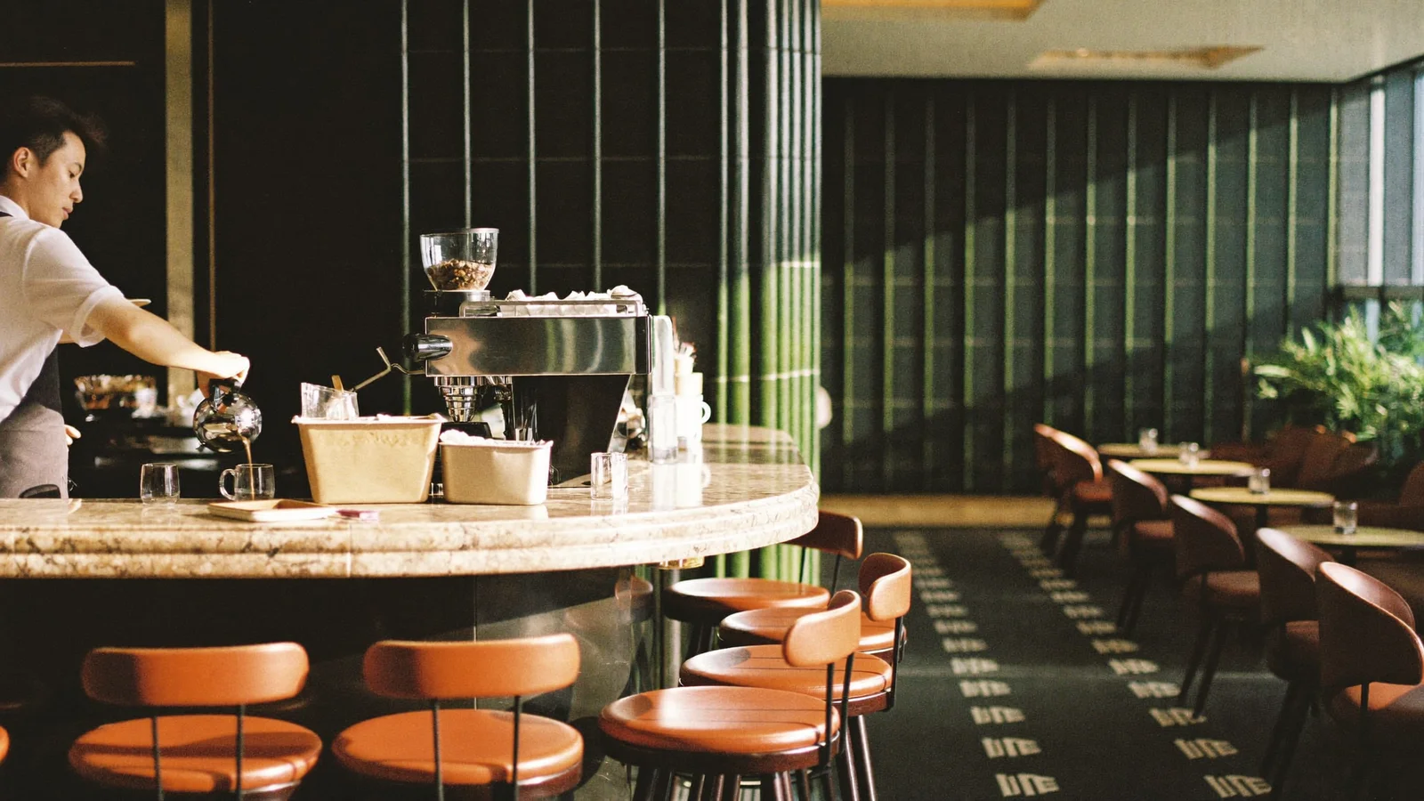 A marble-topped coffee bar with a barista preparing a pour-over coffee, sunlit lounge banquettes in the background of a five-star hotel lobby, illustrative image for this Mandarin Oriental Landmark coffee lounge guide, not a photo of the actual venue or staff