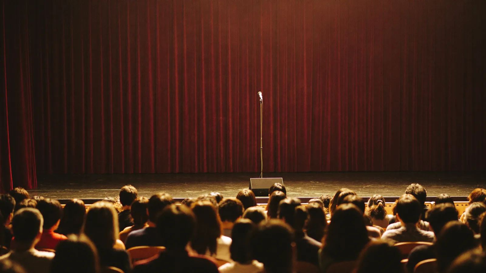 Illustrative image of a spotlit stand-up comedy stage with a microphone stand facing a packed indoor arena audience in Hong Kong, not a photo of Trevor Noah or the actual MacPherson Stadium show