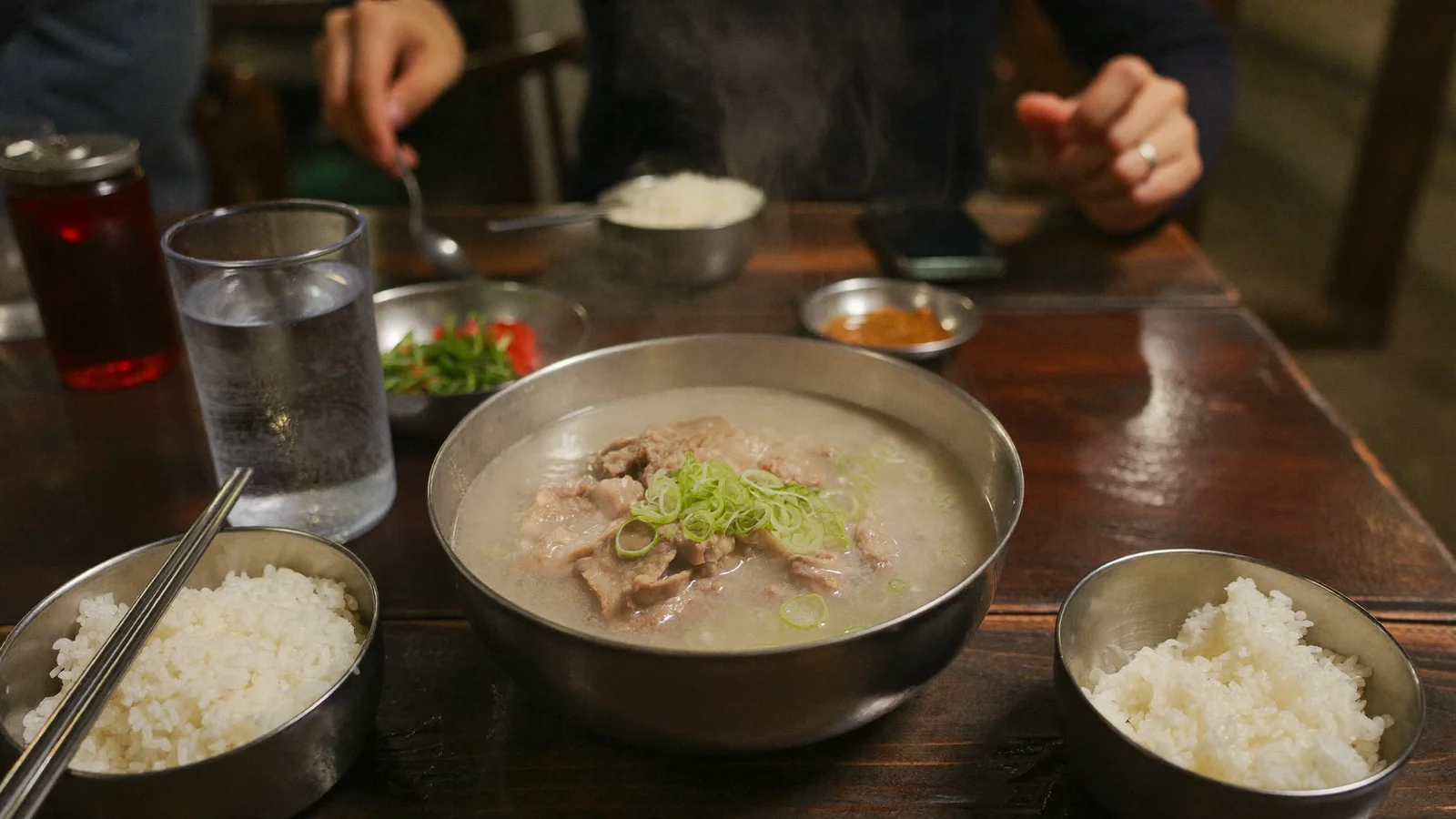 木桌上一碗熱騰騰嘅奶白色韓式豬骨湯，配白飯同蔥花，示意釜山式豬肉湯飯 —— 此為示意圖片，並非該餐廳嘅實照