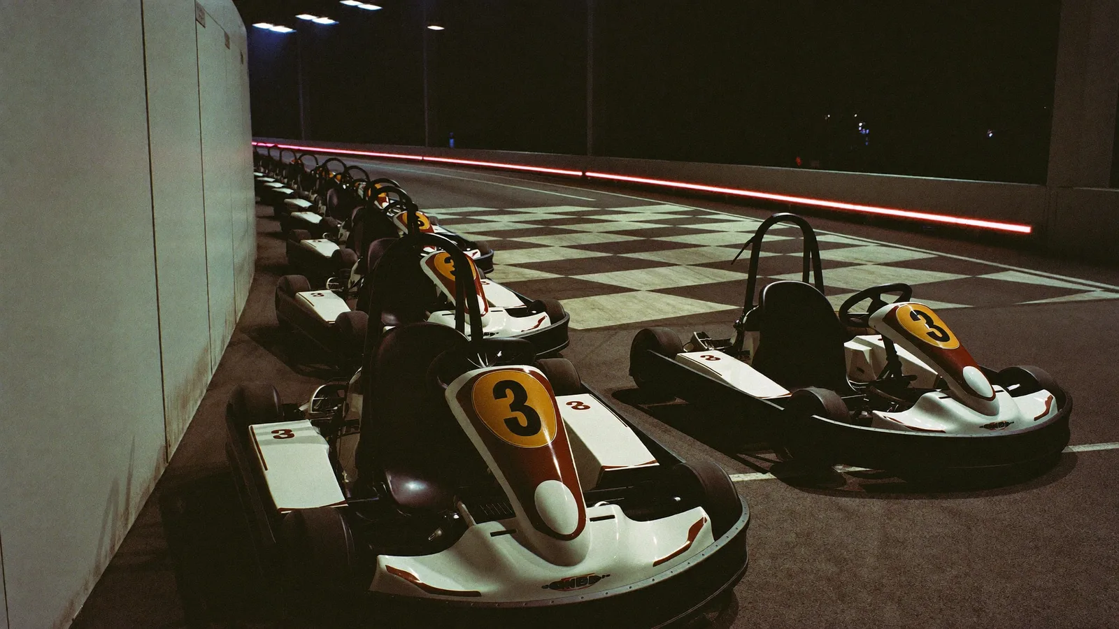A row of empty go-karts with number decals parked on an indoor racing track under bright overhead lighting, illustrating a guide to go-karting venues in Hong Kong - an illustrative image, not a photo of any specific venue