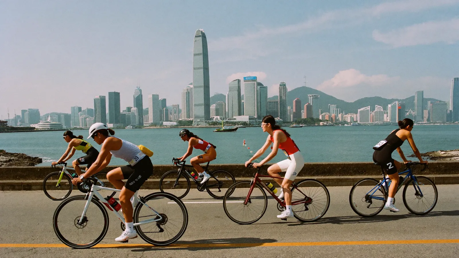 Triathletes cycling along a waterfront road with Hong Kong Island skyscrapers and Victoria Harbour in the background, illustrative image for this World Triathlon Cup Hong Kong 2026 guide, not a photo of the actual event or athletes