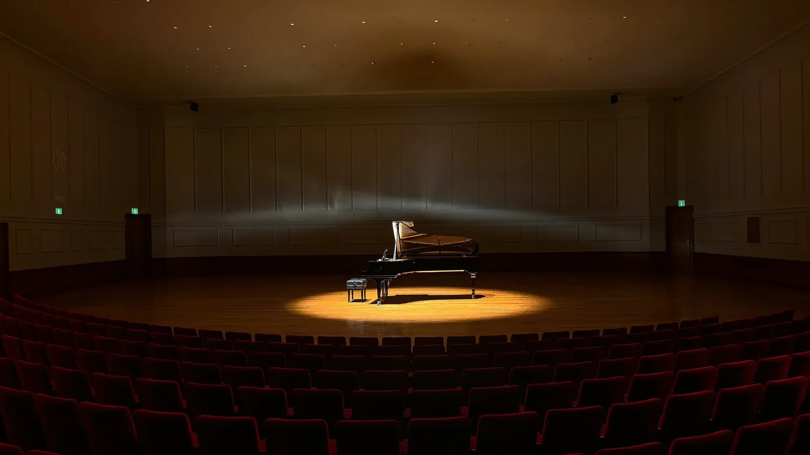 A grand piano lit by a single warm spotlight on an empty concert hall stage, rows of red velvet seats in shadow, illustrative image for this HK Phil National Day concert guide, not a photo of the actual venue or performance
